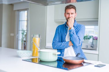 Yakışıklı adam mutfakta İtalyan spagetti makarna pişirme stresli ve ağız tırnakısırma elleri ile sinirli görünümlü. Anksiyete sorunu.
