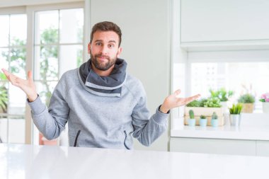 Yakışıklı adam ev clueless ve şaşkın bir ifadeyle kollar ve eller kaldırdı. Şüphe kavramı.