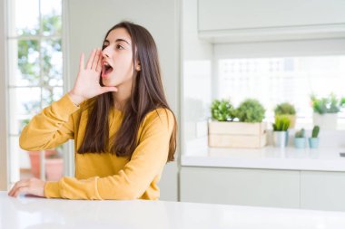 Güzel genç kadın sarı kazak giyen bağırarak ve ağız da el ile yan yüksek sesle bağırıyor. İletişim kavramı.