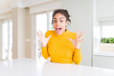 Afro saç ile güzel Afrikalı Amerikalı kadın bir rahat sarı kazak deli kutluyor ve başarı için hayran silah kaldırdı ve açık gözleri heyecanlı çığlık. Kazanan kavramı