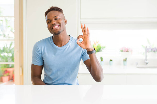 Handsome african american man wearing casual t-shirt at home smiling positive doing ok sign with hand and fingers. Successful expression.