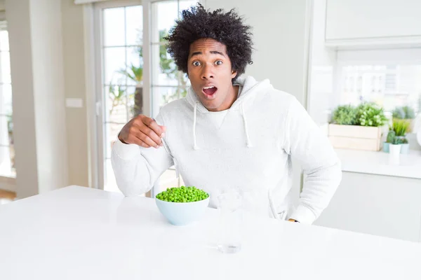 African American man eating fresh green peas at home scared in shock with a surprise face, afraid and excited with fear expression