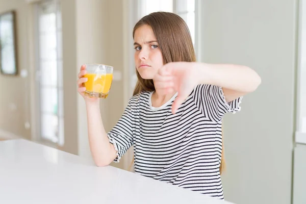 怒った顔で新鮮なオレンジジュースのグラスを飲む美しい若い女の子の子供 親指を下に嫌いを示す否定的な兆候 拒絶概念 — ストック写真