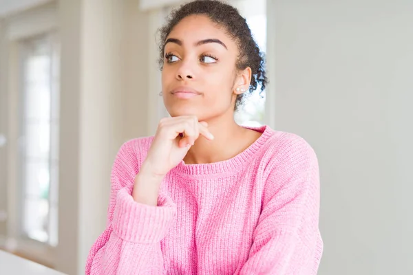 Beautiful young african american woman with afro hair with hand on chin thinking about question, pensive expression. Smiling with thoughtful face. Doubt concept.