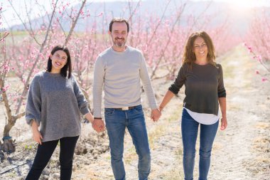 Üç neşeli yürüyüş toghether şeftali bahçesinde bahar güneşli gün zevk pembe yaprakları ile gülümseyen güzel aile