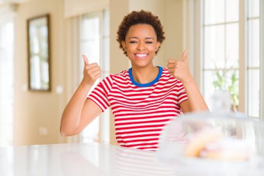 Ev başarı işareti genç güzel Afrikalı Amerikalı kadın el ile olumlu jest yapıyor, gülümseyen ve mutlu yukarı başparmak. Neşeli ifade ile kamera bakarak, kazanan jest.