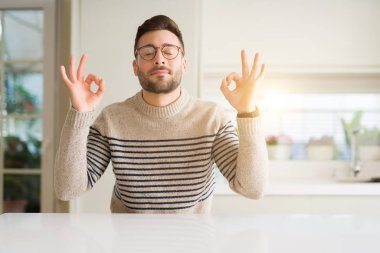 Genç yakışıklı adam gözlük evde dinlenmek ve gülümseyen gözlerle parmak ile meditasyon jest yapıyor kapalı. Yoga kavramı.
