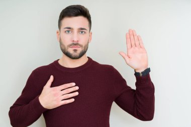 Soyutlanmış arka planda süveter giyen genç yakışıklı bir adam. Elleri göğsünde ve avuçları açık yemin ediyor. Sadakat yemini ediyor.