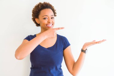 Beyaz arka plan üzerinde genç güzel afro-amerikan kadın şaşırttı ve el ile sunarken kameraya gülümseyerek ve parmak ile işaret.