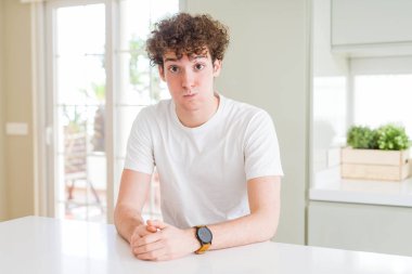 Evde beyaz tişört giyen, komik suratlı, yanak şişiren genç yakışıklı bir adam. Havayla şişmiş ağız, çılgın bir ifade..