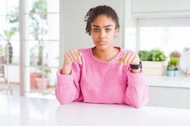 Güzel African Amerikan kadın ile afro saç giyen Casual pembe kazak üzgün ve üzgün görünümlü aşağı Işaret, parmaklarla yönü gösteren, mutsuz ve depresif.