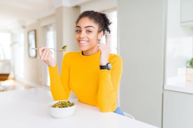 Sağlıklı yeşil sebze yeme genç Afrikalı Amerikan kadın bir fikir veya soru mutlu yüz, bir numara ile parmak işaret ile şaşırdı