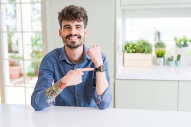 Beyaz masada oturan rahat gömlek giyen genç adam acele seyretmek zaman, sabırsızlık, üzgün ve son gecikme için kızgın işaret