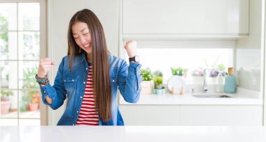 Güzel Asyalı kadın beyaz masa üzerinde denim ceket giyen silah ile başarı için heyecanlı kutlamak zafer gülümseyen kaldırdı. Kazanan kavramı.