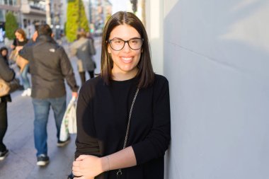 Şehir sokaklarında yürürken heyecanlı gülümseyen güzel genç esmer kadın, şehirde açık havada mutlu ve güven ifade ayakta