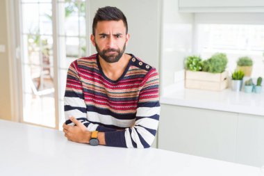 Yakışıklı İspanyol adam evde çizgili kazak giyen şüpheci ve sinirli, çapraz kolları ile yüzünde onaylamayan ifade. Negatif kişi.