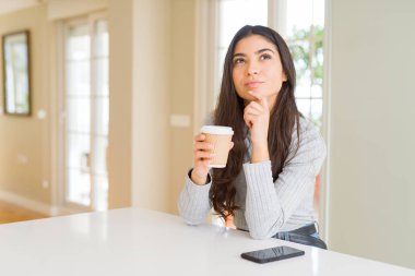 Bir fincan kahve içen genç bir kadın. Ciddi bir yüz ifadesi. Soru soran, kafası karışık bir fikir.