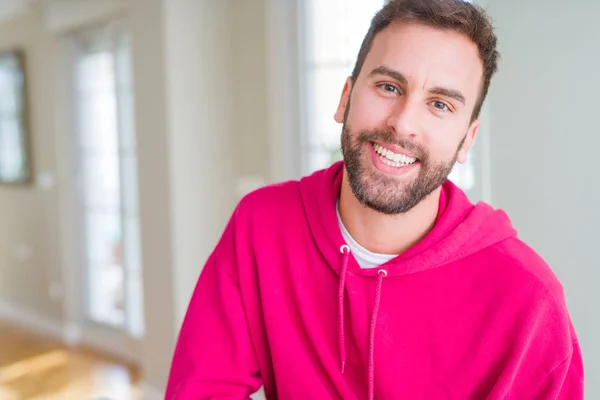 Hombre guapo vistiendo sudadera casual en casa y sonriendo —  Fotos de Stock