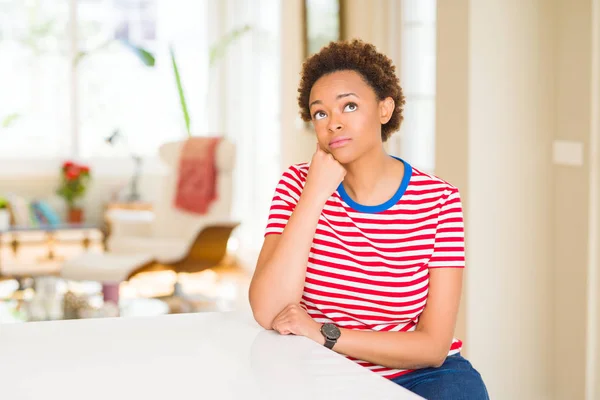 Young beautiful african american woman at home with hand on chin thinking about question, pensive expression. Smiling with thoughtful face. Doubt concept.