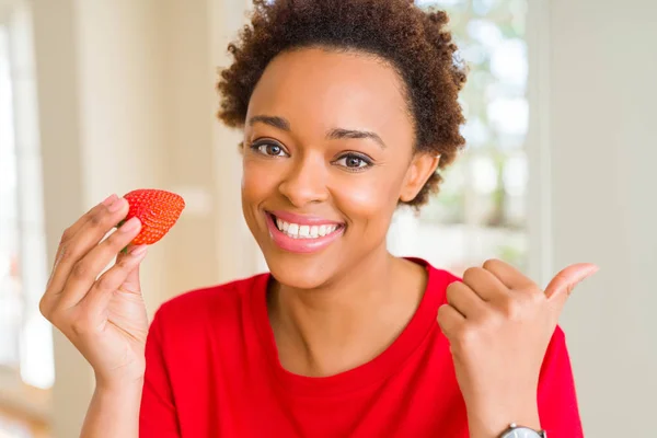 若いアフリカ系アメリカ人女性は 朝食のために新鮮なイチゴを食べて 幸せな顔をして横に親指で示しています — ストック写真