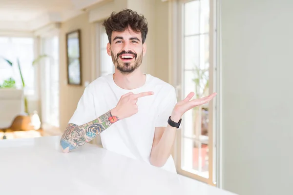 Jovem Vestindo Camiseta Casual Sentado Mesa Branca Maravilhado Sorrindo Para — Fotografia de Stock