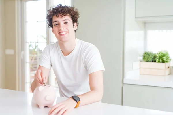 Молодой Человек Вкладывает Деньги Используя Копилку Дома Счастливым Лицом Стоя — стоковое фото
