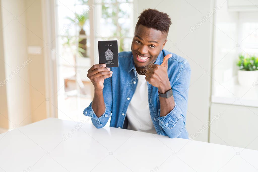 African american man holding passport of Canada happy with big smile doing ok sign, thumb up with fingers, excellent sign