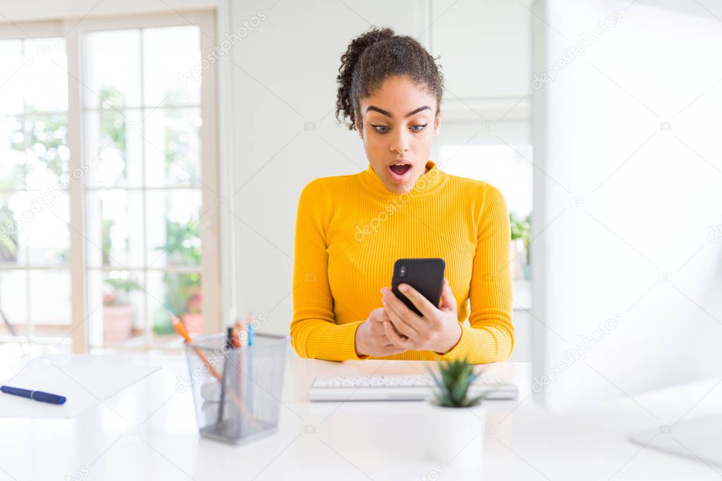 Young african american girl working using computer and smartphone scared in shock with a surprise face, afraid and excited with fear expression