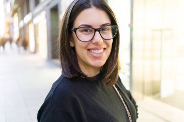 Şehir sokaklarında yürürken heyecanlı gülümseyen güzel genç esmer kadın, şehirde açık havada mutlu ve güven ifade ayakta