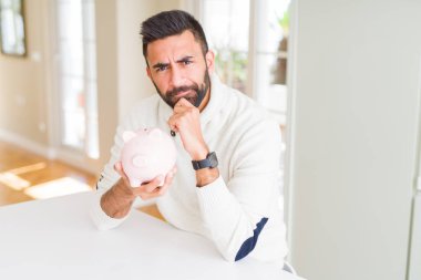 Yakışıklı İspanyol adam kumbara tutan ciddi yüz soru hakkında düşünme, çok karışık bir fikir