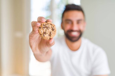 Ayakta ve diş gösterilen kendine güvenen bir gülümsemeyle gülümseyerek mutlu bir yüz ile çerezleri yakışıklı İspanyol adam yeme çikolata cips
