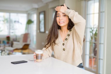 Evde bir fincan kahve içen genç kadın, eliyle başını gerdi, utanç ve sürpriz yüzle şoke oldu, kızgın ve hüsrana uğradı. Korku ve hata için üzgün.
