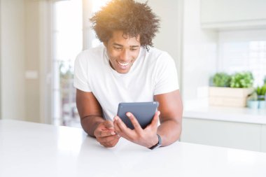 Afro-Amerikan adam ayakta mutlu bir yüz ile touchpad masa kullanarak ve dişleri gösteren kendinden emin bir gülümseme ile gülümseyerek