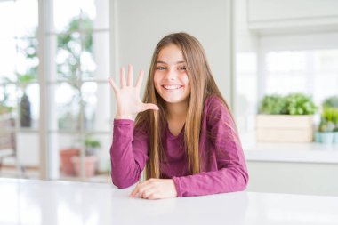 Beyaz masa üzerinde güzel genç kız çocuk gösteren ve parmakları ile işaret ederken beş numara kendinden emin ve mutlu gülümseyerek.