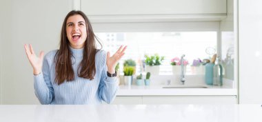 Evde beyaz masada oturan güzel genç kadının geniş açılı resmi deli ve deli bağırarak ve agresif ifade ve kollar kaldırdı ile bağırıyor. Hayal kırıklığı kavramı.