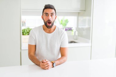 Yakışıklı İspanyol adam evde rahat beyaz t-shirt korkmuş ve sürpriz ifade ile şok, korku ve heyecanlı yüz.