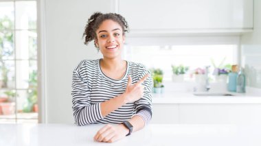 Afro saçlı güzel Afrikalı Amerikan kadın, mutlu ve doğal ifade ile yan kadar el ve parmak ile işaret yüzü bir gülümseme ile rahat çizgili kazak neşeli giyiyor