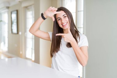 Rahat beyaz t-shirt giyen güzel genç kadın mutlu yüzü ile elleri ve parmakları ile çerçeve yapma gülümseyerek. Yaratıcılık ve fotoğrafçılık konsepti.