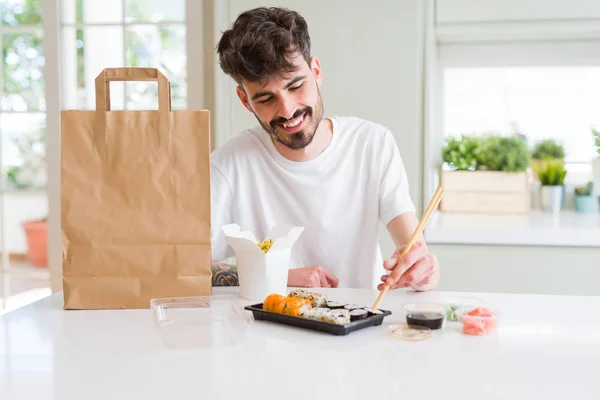 Young man eating sushi asian food and noodles using choopsticks from take away delivery