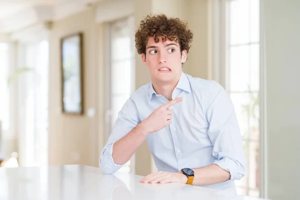 Young business man with curly read head Pointing aside worried and nervous with forefinger, concerned and surprised expression