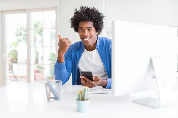 スマートフォンとコンピュータを使って働くアフリカ系アメリカ人男性が 笑顔で親指を立てて顔を出す — ストック写真