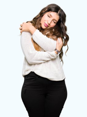 Kendini mutlu ve olumlu sarılma, kendinden emin gülümseyen beyaz kazak giyen genç güzel kadın. Kendi aşk ve öz bakım