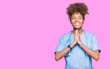 Young african american doctor woman over isolated background praying with hands together asking for forgiveness smiling confident. clipart