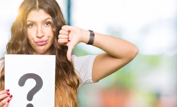 怒った顔で疑問符が付いた紙を持つ若い成人女性 親指を下にして嫌いを示す否定的なサイン 拒絶概念 — ストック写真