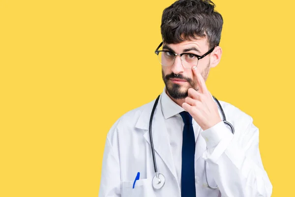 Young doctor man wearing hospital coat over isolated background Pointing to the eye watching you gesture, suspicious expression