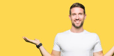 Casual beyaz t-shirt gülen iki elle gösterilen giyen yakışıklı adam açık avuç içi, sunmak ve reklam karşılaştırma ve denge