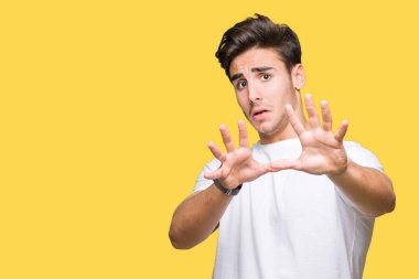 Şokta bağırarak korkuyor ve dehşet korku ifade dur hareketi el ile ile izole arka plan üzerinde beyaz t-shirt giyen genç yakışıklı adam. Panik kavramı.