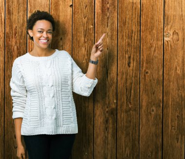 Kameraya bakarak yan el ve parmak ile işaret Kazak yüzünde kocaman bir gülümseme ile izole arka plan üzerinde giyen güzel genç Afro-Amerikan kadın.