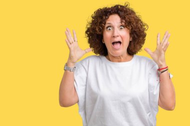 Üzerinde beyaz t-shirt giyen güzel orta ager üst düzey kadın deli kutluyor arka plan izole ve başarı için kaldırdı kollarını açarak hayrete ve heyecanlı çığlık gözleri açık. Kazanan kavramı