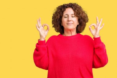 Güzel orta ager üst düzey kadın kırmızı kış kazak izole arka plan üzerinde dinlenmek ve gülümseyen gözlerle kapalı parmak jestle meditasyon yapıyor. Yoga kavramı.